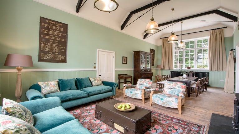 The open plan sitting and dining area at Crabtree School House, Devon. The sitting area next to the dining area has two large sofas and two chairs.